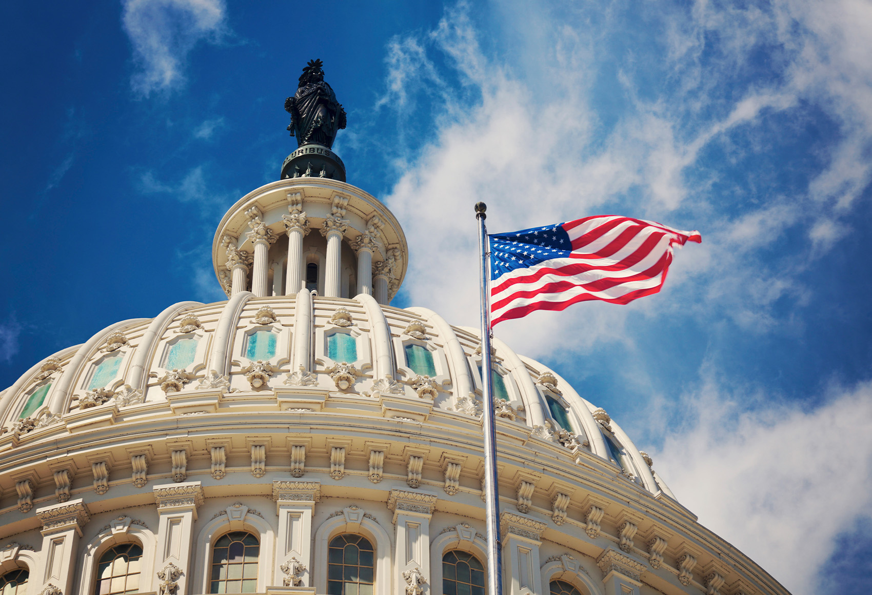 United States Capitol building with flag and sky in foreground and background