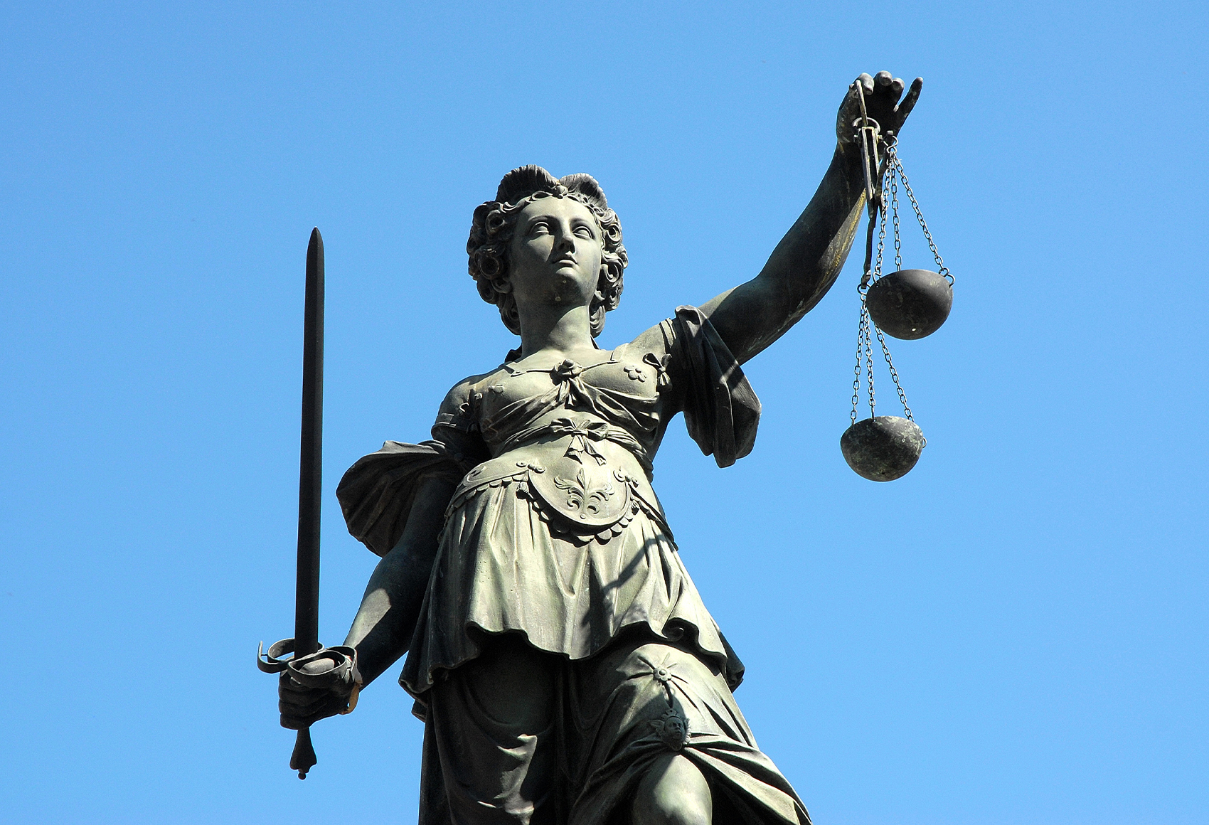 A low-angle, close-up shot of a statue of Lady Justice against a clear blue sky.
