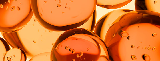 Abstract close-up of translucent orange spheres with tiny bubbles suspended inside against a golden background.