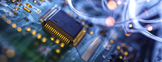Close-up of a microchip on a blue circuit board with gold connections and glowing fiber-optic strands.