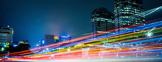 image is a long-exposure photograph showing light trails from vehicular traffic moving along a city street at night