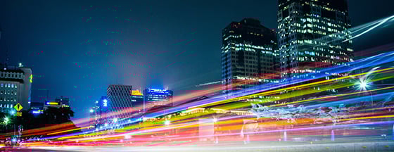 image is a long-exposure photograph showing light trails from vehicular traffic moving along a city street at night