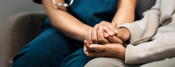 Healthcare provider in scrubs holding the hand of a patient on a sofa