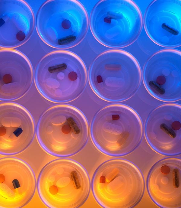 Overhead view of pills and capsules in a grid of clear circular compartments, lit orange on the left and blue on the right.