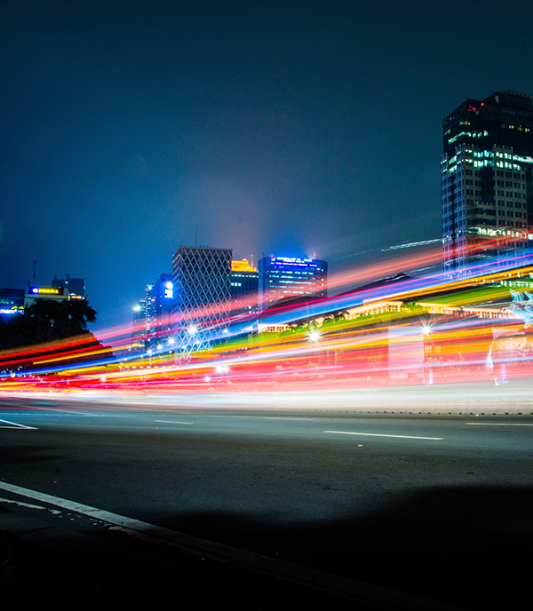 image is a long-exposure photograph showing light trails from vehicular traffic moving along a city street at night