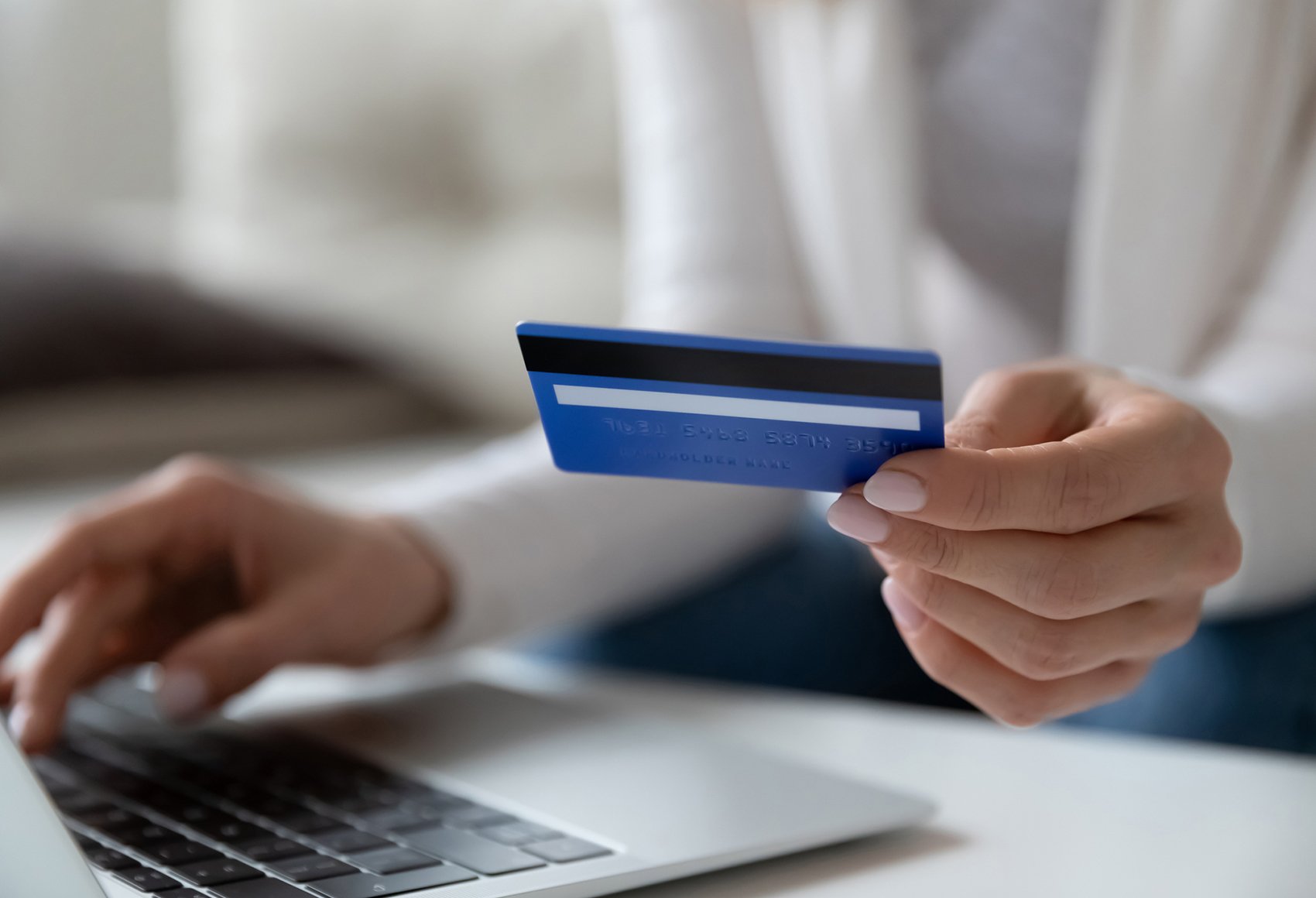 A woman's hand holding a bank card and inserting the details of the card into her laptop